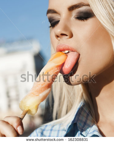 stock_photo_closeup_of_a_pretty_woman_licking_an_ice_cream_against_the_background_of_the_blue_sky_the_girl_in_162308831.jpg