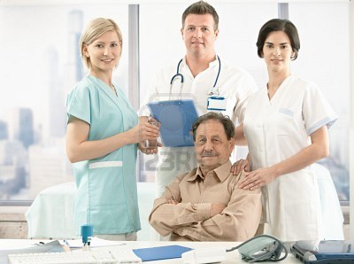 7653609_portrait_of_senior_patient_sitting_at_desk_medical_team_around_smiling_at_camera.jpg